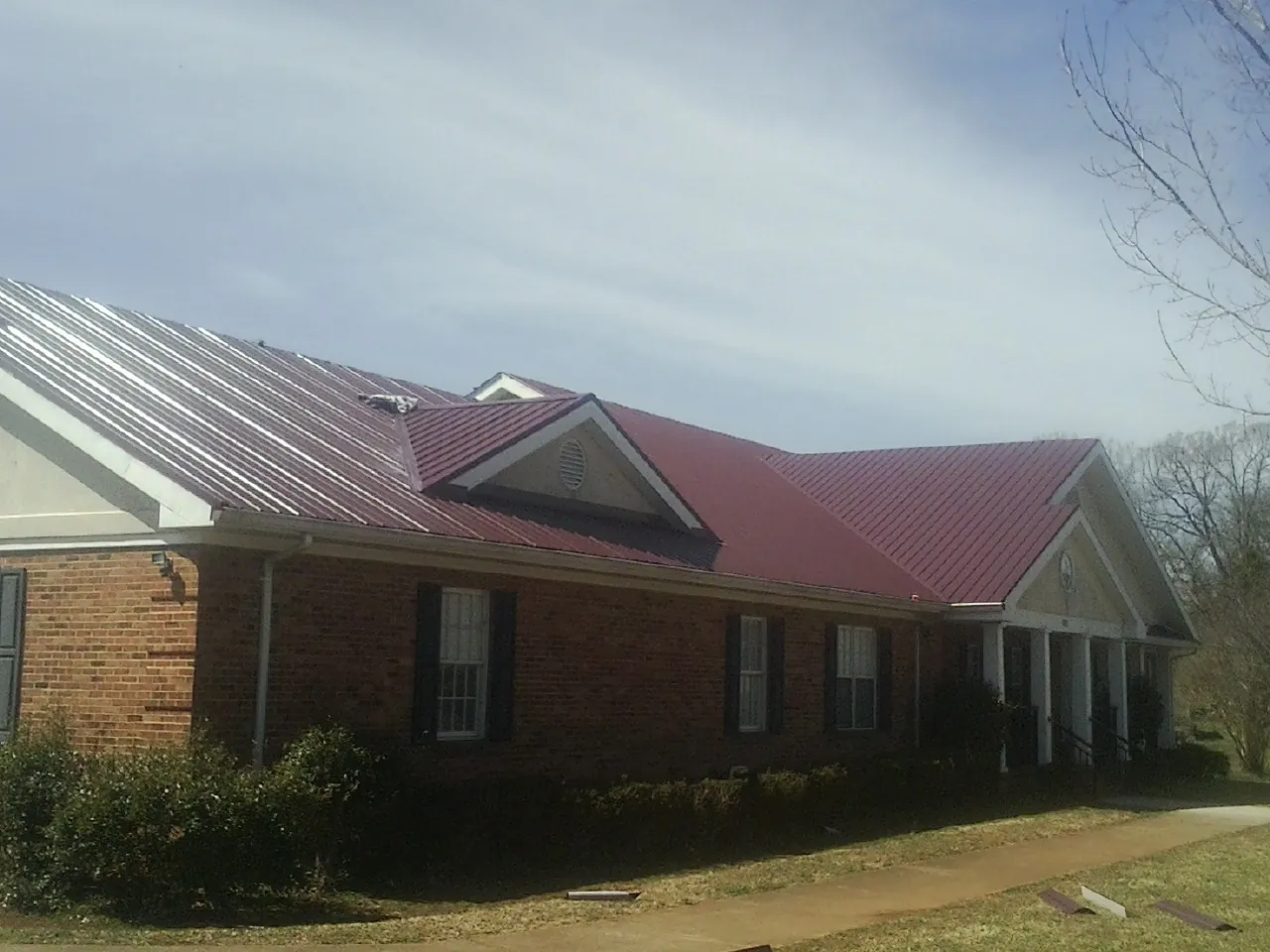 Red metal roof with gabled entries on a long brick building, from a Hail Damage Roof Repair job in Kenai