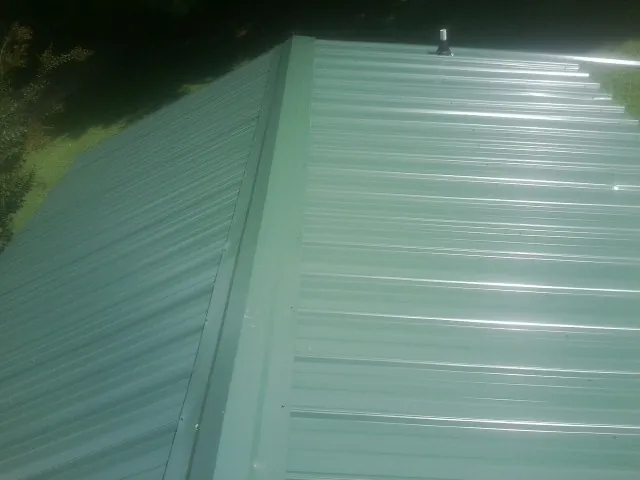 New green metal panels meeting at the ridge of a roof — Flat Roof Repair work by our crew in Kenai