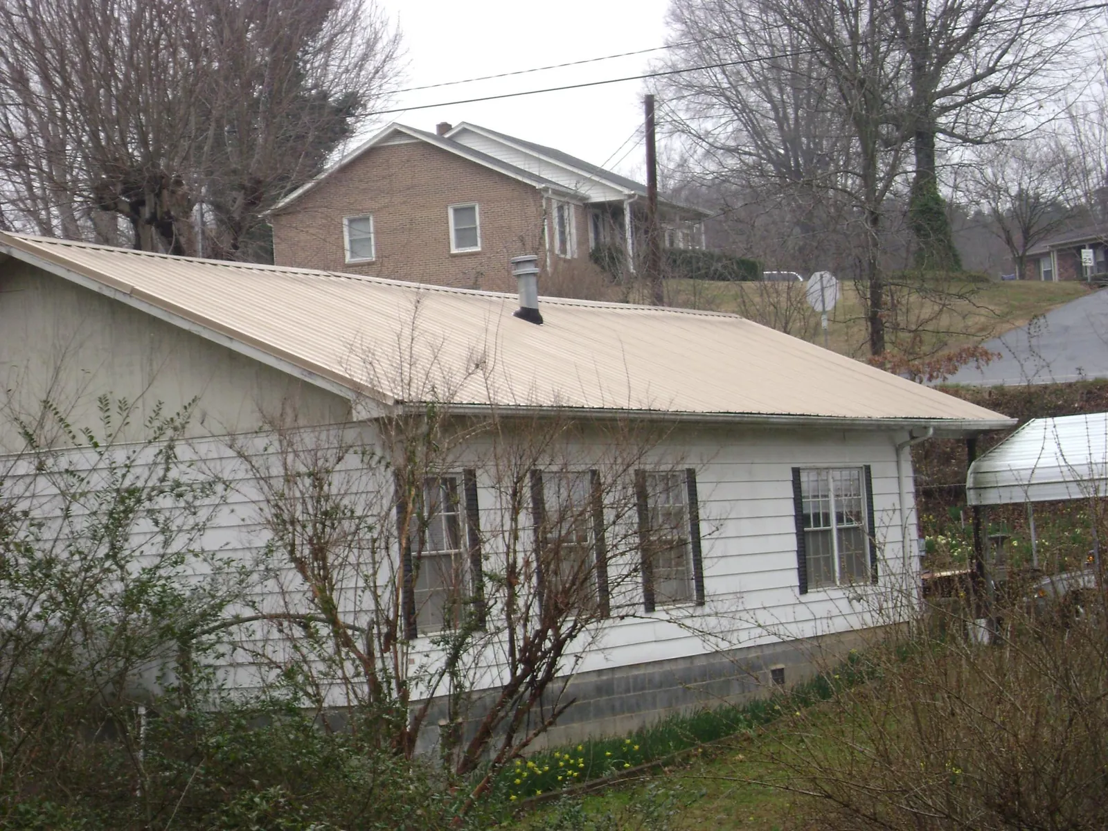 Tan metal roof on a white sided house set into a hillside — Commercial Roofing by Roofing Brothers in Kenai