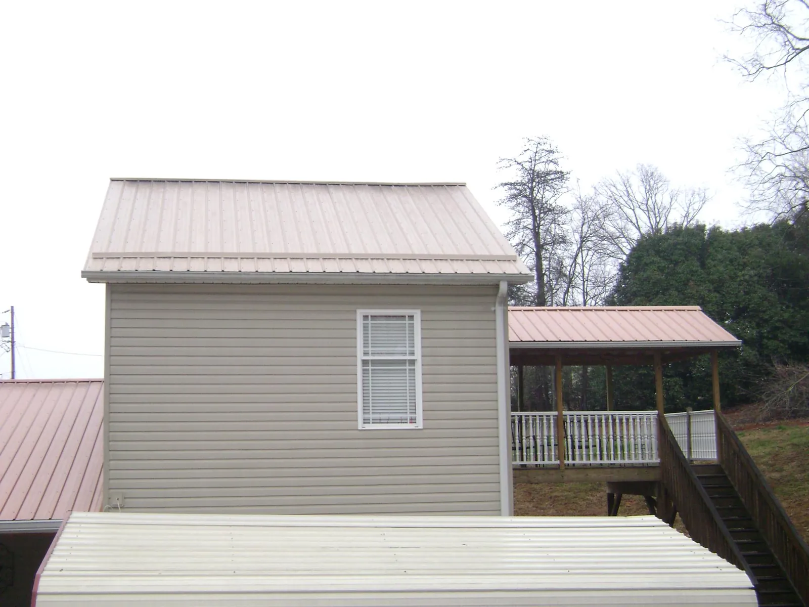 Tan metal roofs on a two story addition and attached porch, from a Roof Replacement job in Kenai