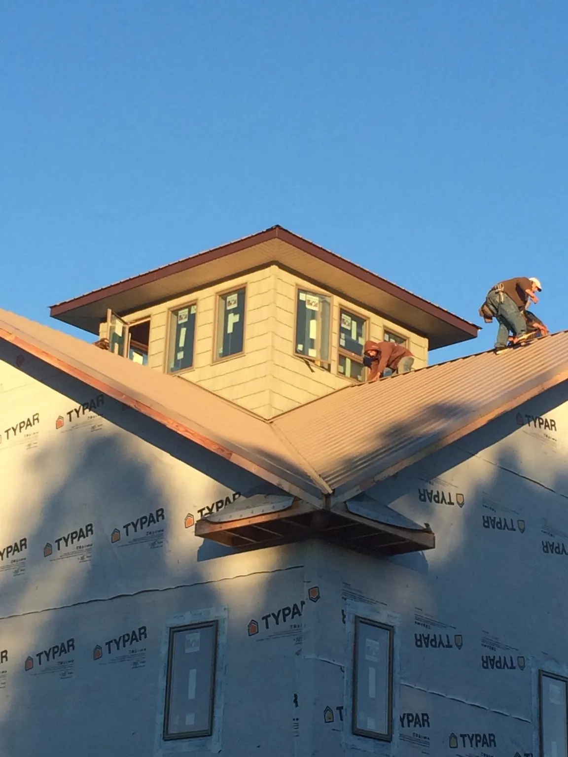 Roofers working around a rooftop cupola on a new metal roof at sunset — Roof Waterproofing in Kenai by Roofing Brothers